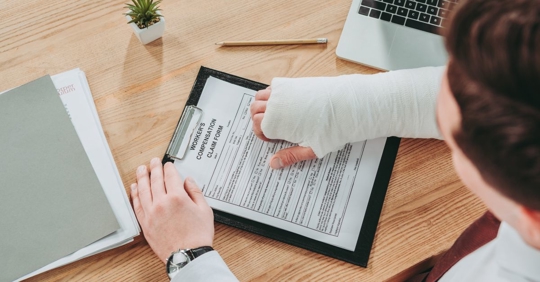 Worker holding broken arm compensation claim and sitting at table in office